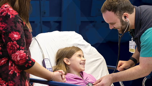 A man and a woman stand beside a young girl laying on a hospital bed, highlighting the compassionate medical care she is receiving in a warm setting.