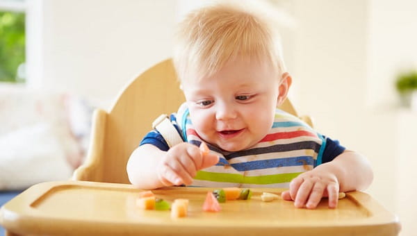 Baby Boy Eating Fruit In High Chair