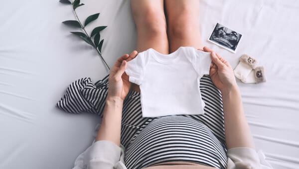 a pregnant woman sitting down holind a baby sized shirt