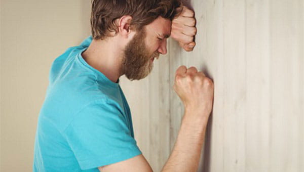 A man leaning with clenched fists against a wall.