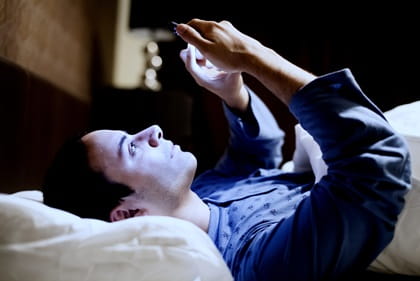 A man is checking his cellphone while in bed