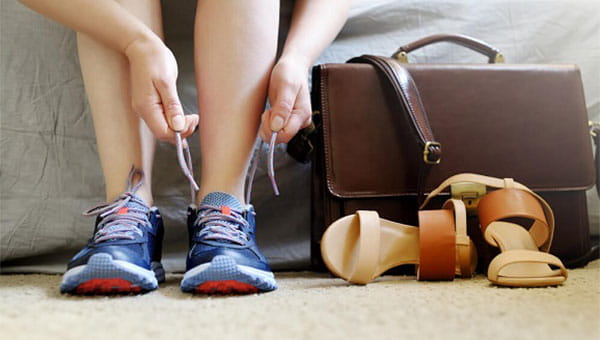 person tying a shoe next to a purse.