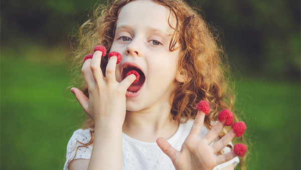 A young girl is eating raspberries that she placed on her fingertips