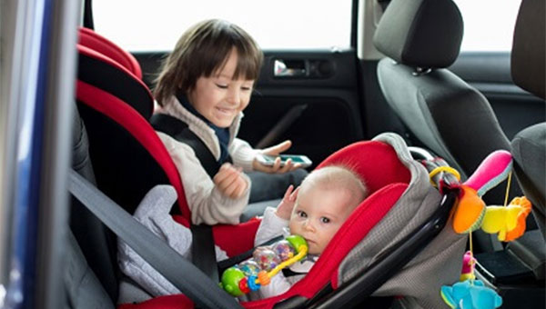 Older child in a forward facing car seat with their toddler sibling is in a rear facing car seat