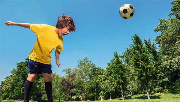 A boy playing soccer and hitting the soccer ball off the top of his head