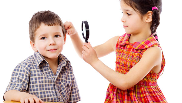 A young girl inspects her friend's ear with a magnifying glass