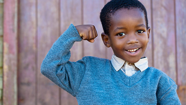 A young boy smiles while flexing his muscles in his right arm