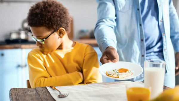 A boy turns his head away from the food his father is placing on the table