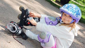 A little is wearing a helmet and putting on her rollerblades.
