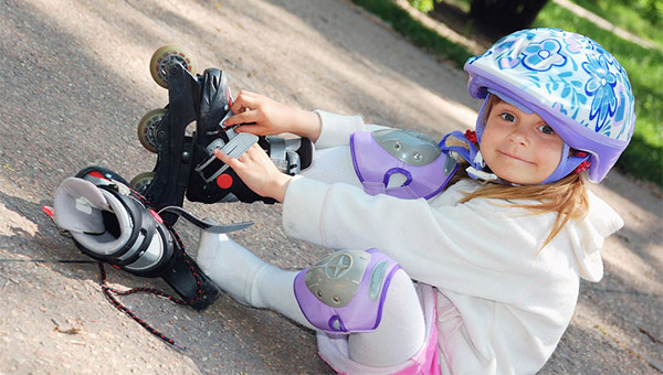Little girl is putting on her rollerblades with a helmet and kneepads on on