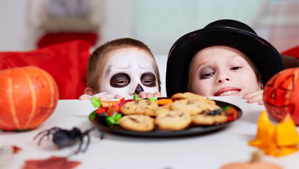 Two children dressed up in Halloween costumes looking at cookies