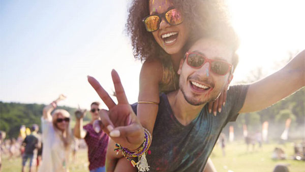 A young woman and young man are wearing sunglasses at an outdoor event on a sunny day.