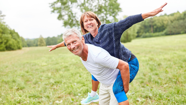 Senior woman rides piggyback on her partner's back in the park in summer