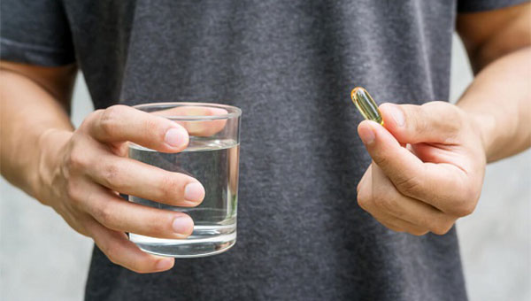 A man is holding a fish oil supplement pill and a glass of water