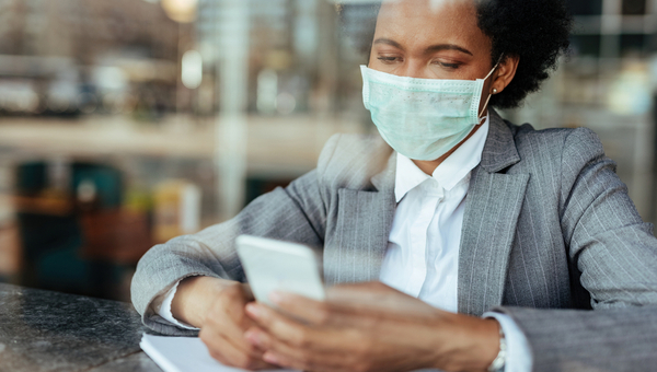 Black businesswoman wearing protective mask on her face while using smart phone and reading text message
