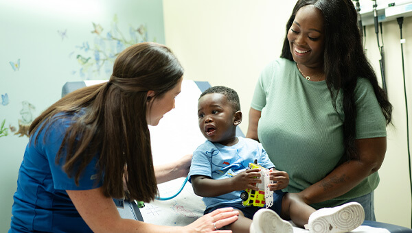 A nurse and small child look at each other while the child's mother smiles in the background.