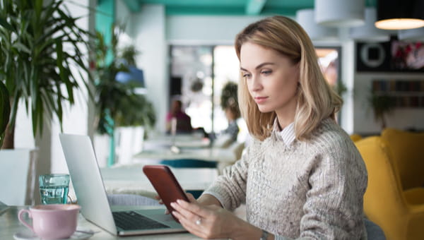 Busy female freelancer reading using mobile device and laptop