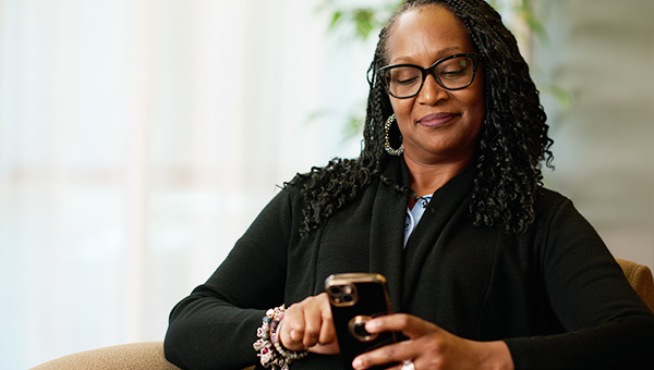 African American lady sitting in a chair scheduling a mammogram on her phone.