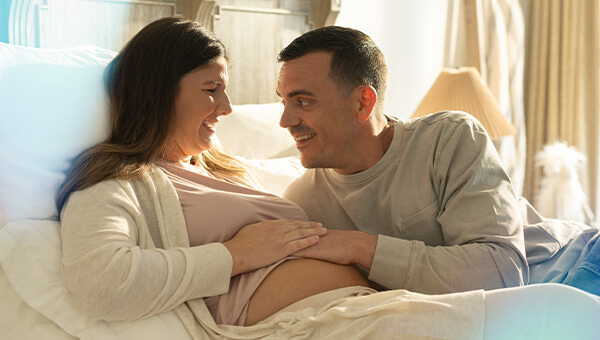 Pregnant woman who is in a hospital bed with a man smiling while both are touching her belly