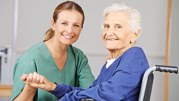 A nurse is sitting next to a male patient who is in a wheelchair.