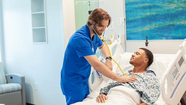 male baycare clinician in baycare scrubs listening to patients heart