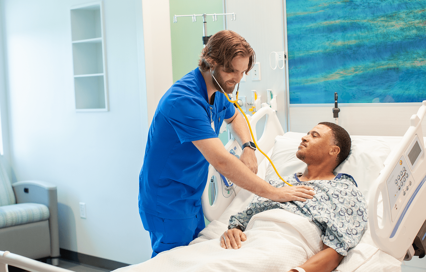 A BayCare nurse in a bright patient room checking a patient heart beat with a stethoscope.