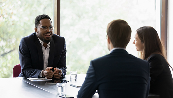 young well dressed professional smiling across the table from his male and female coworkers
