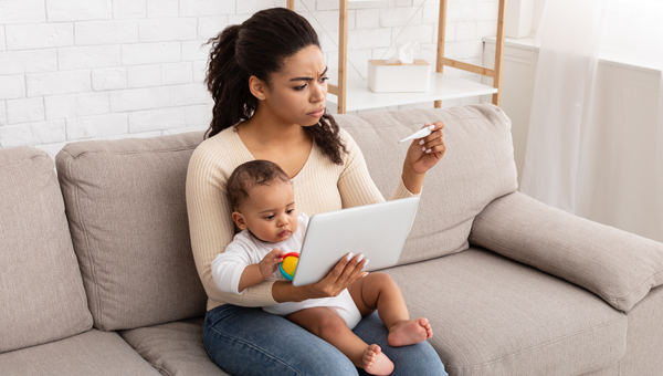 young mother holding newborn on couch and checking thermometer