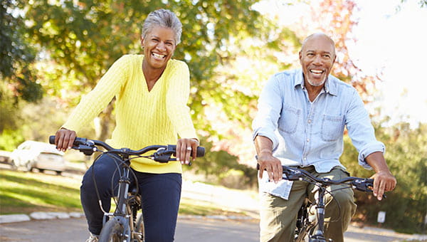 Smiling older man and woman riding bikes in a park.