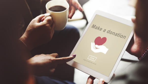 An iPad shows a Make a Donation page with hands pointing toward it. 