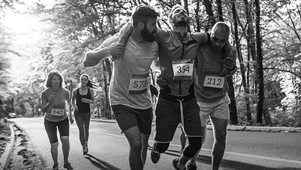 An injured runner is helped by two other runners.