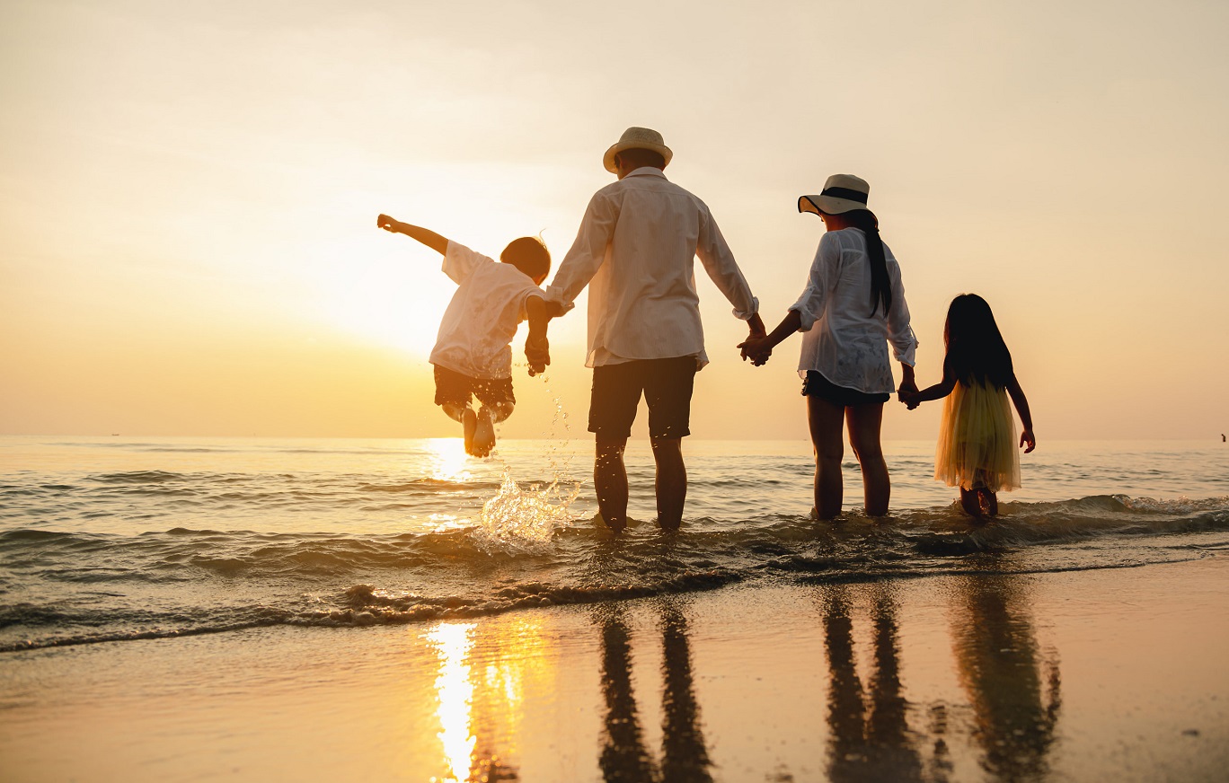 family of four facing the ocean on a beach watching the sun set