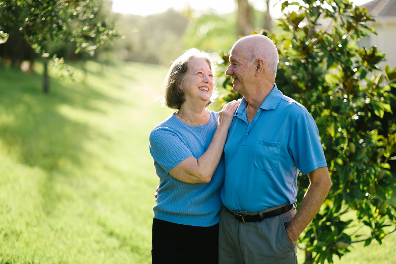 Couple hugging in a park while smiling and standing in front of trees.