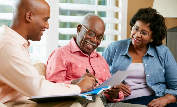 elderly couple smiling and filing out documentation with a counselor