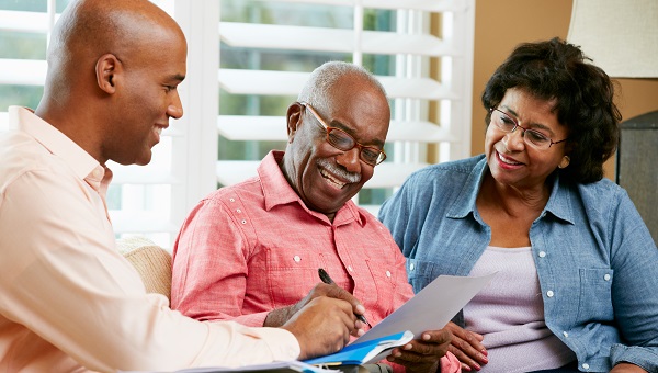 An elderly black man sits between two younger black people while they are reviewing a pamphlet.