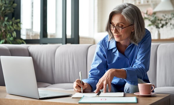 A woman takes notes while looking at a laptop screen.