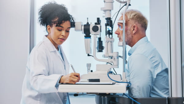 Clarity About Your Vision Benefits Vision, eye exam and writing with a female optometrist testing the eyes of a senior male patient.