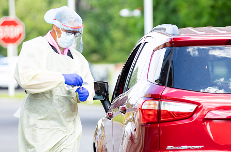 Medical professional standing beside a card at a covid drive through testing center