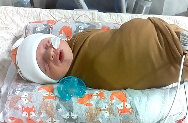 A newborn baby boy in a NICU bed is sleeping. The baby has medical equipment hooked up to him.
