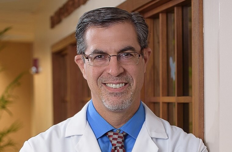 A headshot of Dr. Paul Lewis wearing a white lab coat over a blue dress shirt and tie.