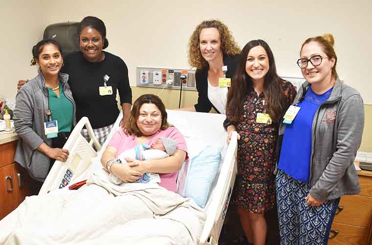 Five smiling doctors surround a new mom holding her baby. 