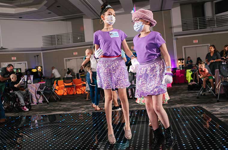 St. Joseph's Children's Hospital patient Dylan is  8 years old and raises hand in the air on the dance floor next to her sister Sadie. Both girls are wearing purple dresses. They are having fun at the hospital's prom.