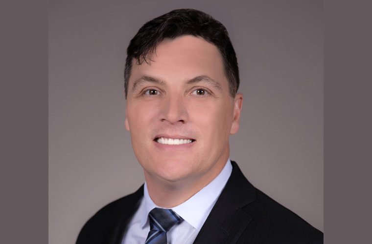 A male with short dark hair is wearing a black suit jacket and smiling in his headshot photo.