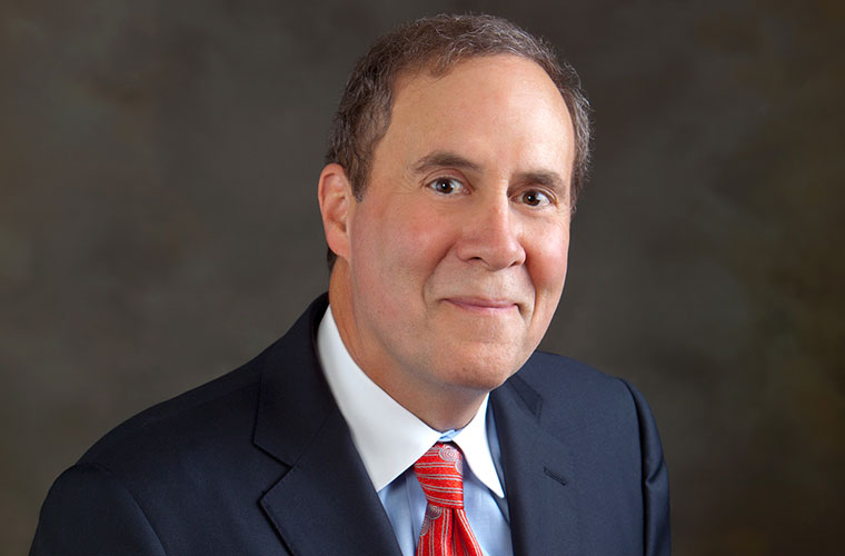 A formal photo of a man wearing a black jacket over a white shirt and red tie.