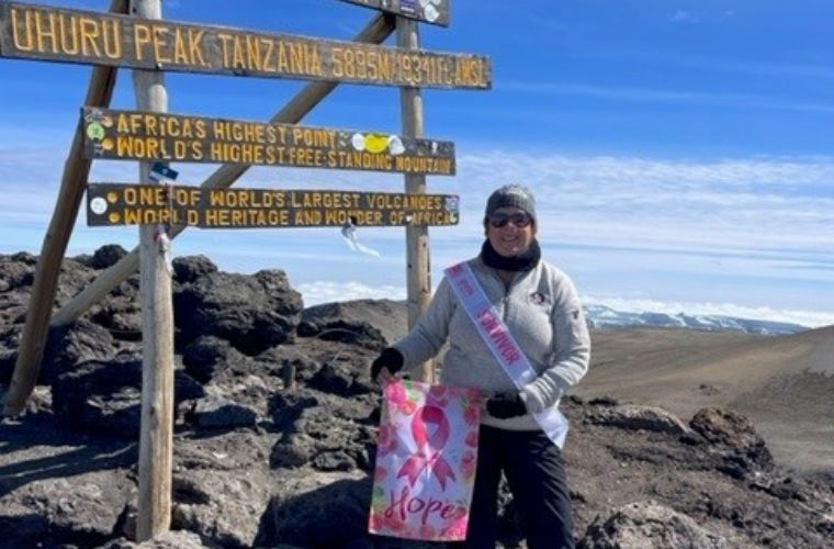 Deborah Sickmon stands proudly at the peak of the mountain holding her pink breast cancer survivor sash. 