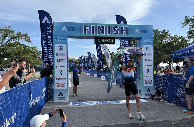 A man dressed in athletic clothing holds the tape after crossing the finish line first in an athletic competition.