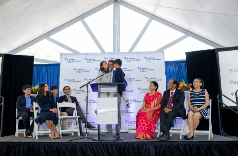 A group of adults and children on a stage in front of a banner that says St. Joseph's Children's Hospital.