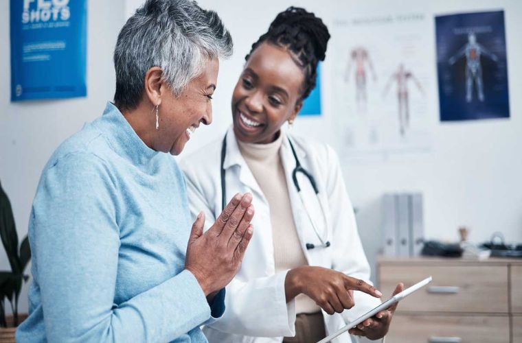 Young Black woman doctor with braided bun treating an older Black female patient with short gray hair.