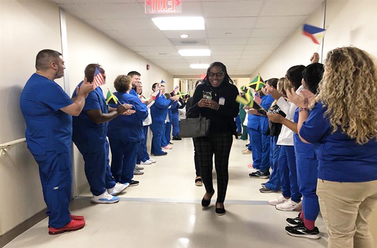 A woman walks down a hallway while other people lined on either side of her applaud her.