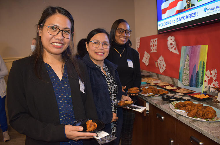 Three women smile at the camera while holding food.